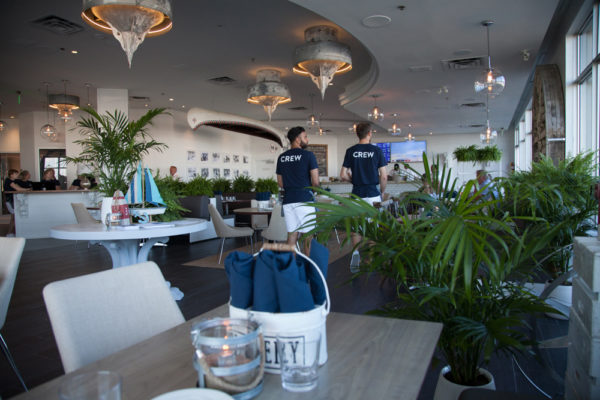 Interior of Bronte Boathouse with many tables and chairs and a bar a the back, and a couple of staff.