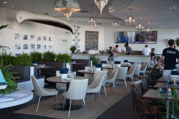 Interior of Bronte Boathouse with many tables and chairs and a bar a the back.